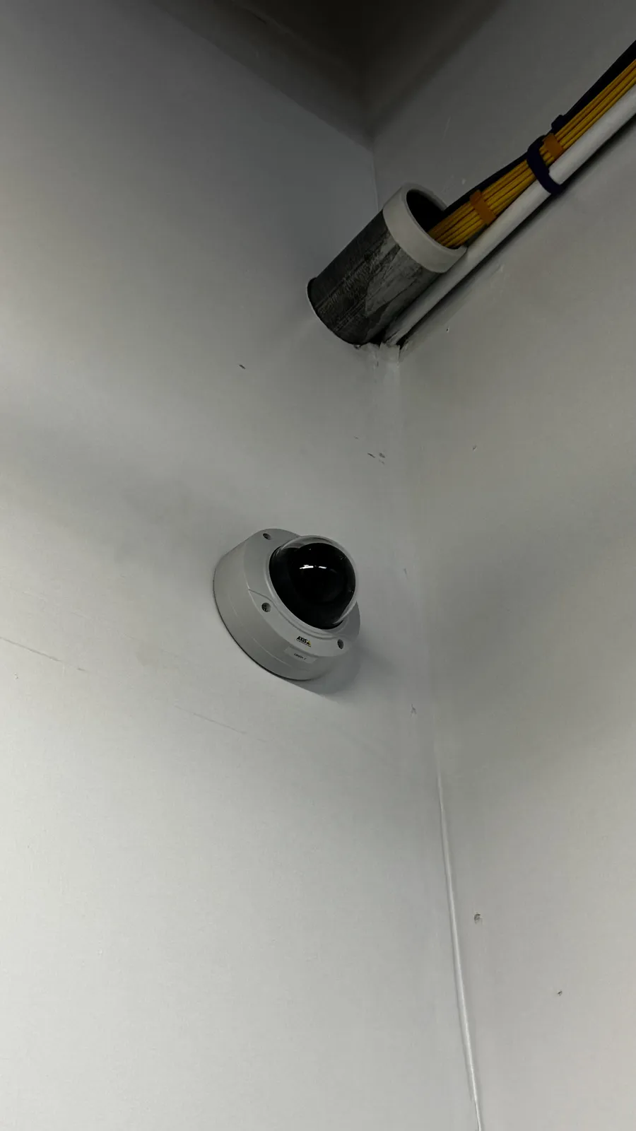 Dome camera mounted in a wall corner with cabling run into conduit above