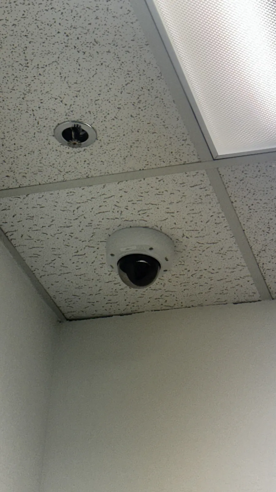 Dome camera set into a drop ceiling tile beside a light fixture